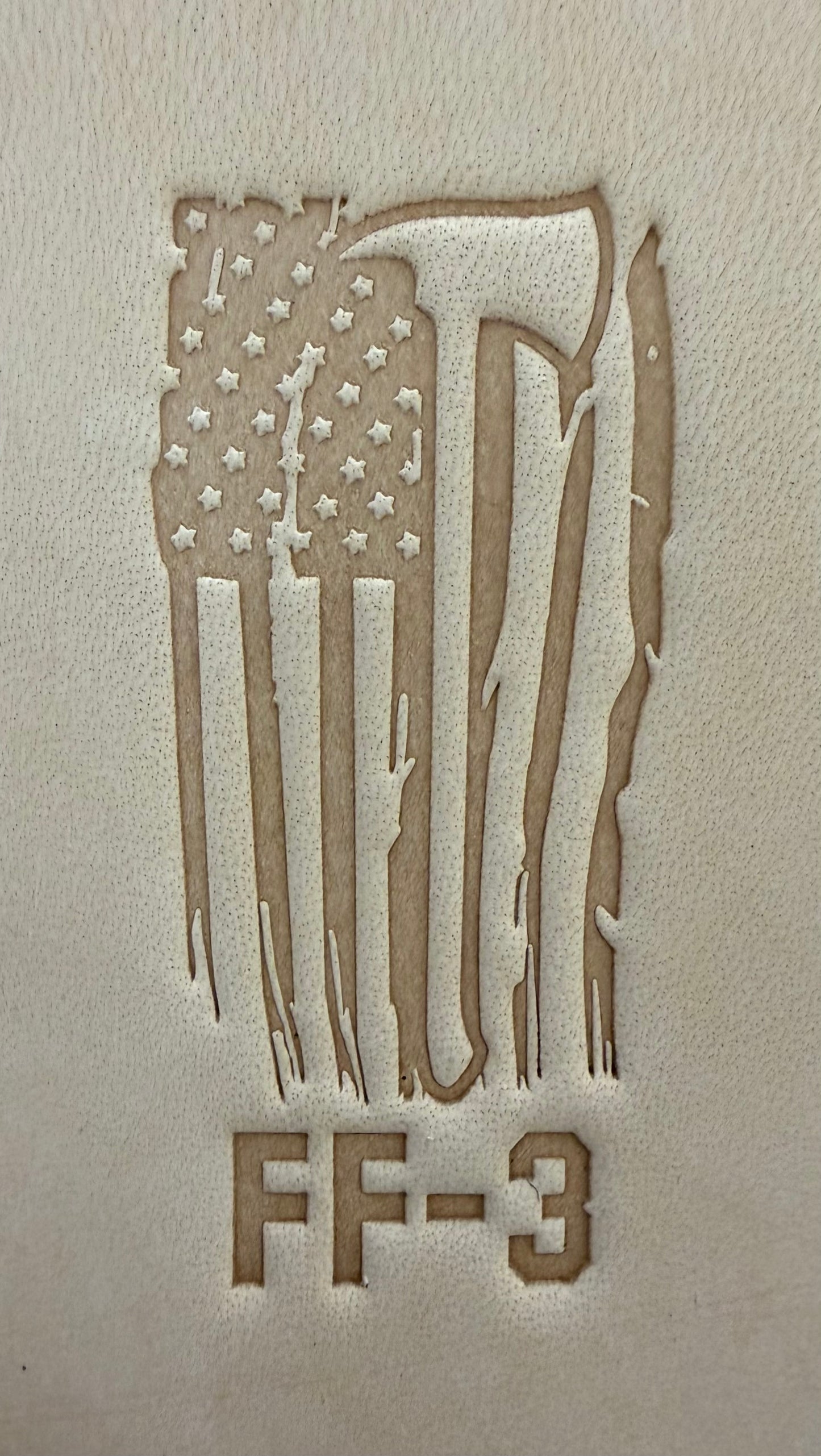 Delrin leather stamp pressing a tattered U.S. flag design with a firefighting axe and Halligan bar into leather.