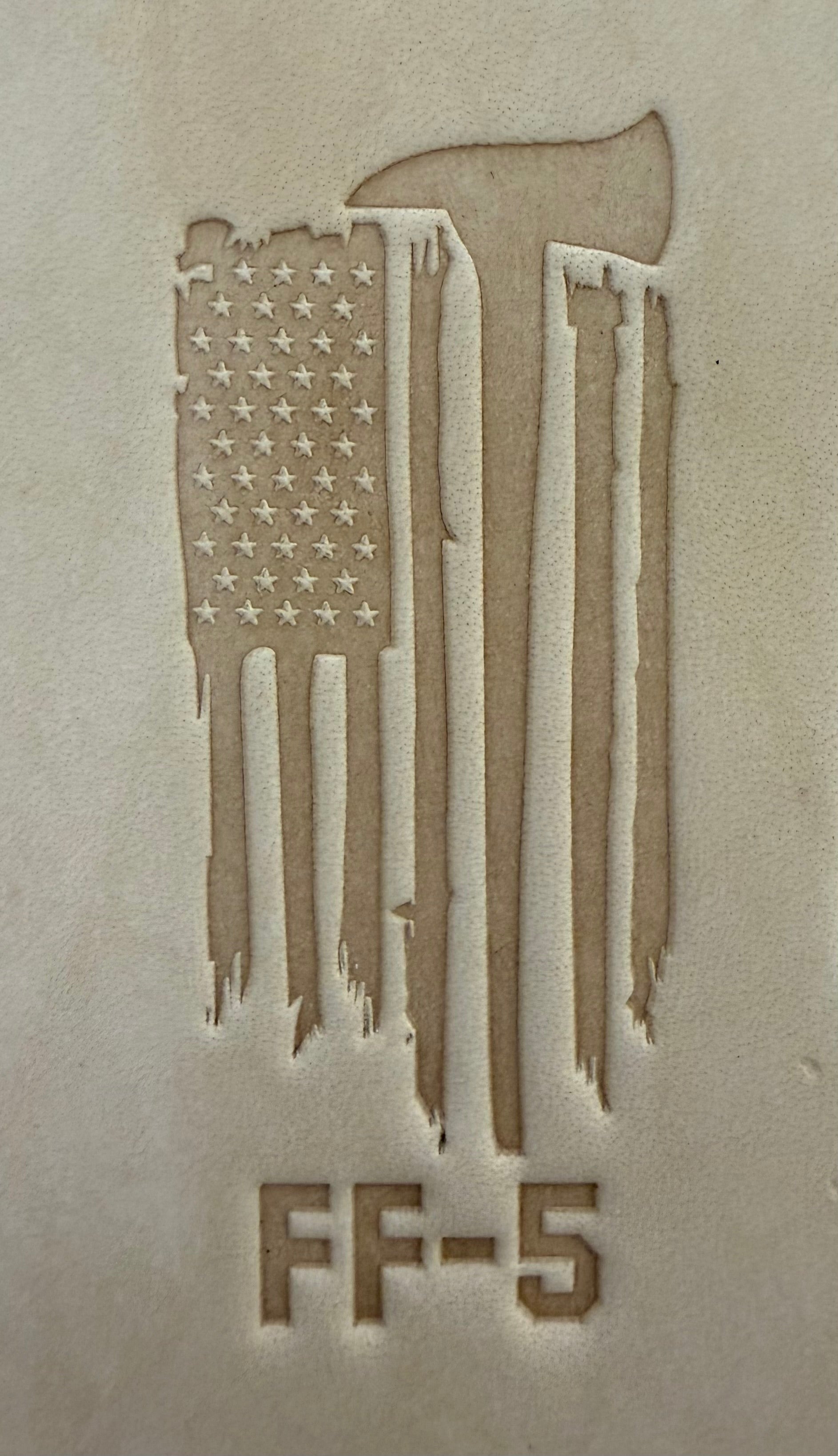 Delrin leather stamp pressing a tattered U.S. flag design with a firefighting axe and Halligan bar into leather.