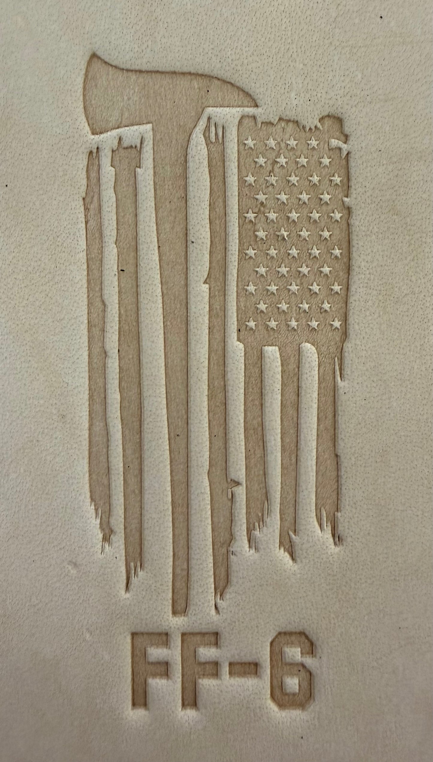 Delrin leather stamp pressing a tattered U.S. flag design with a firefighting axe and Halligan bar into leather.