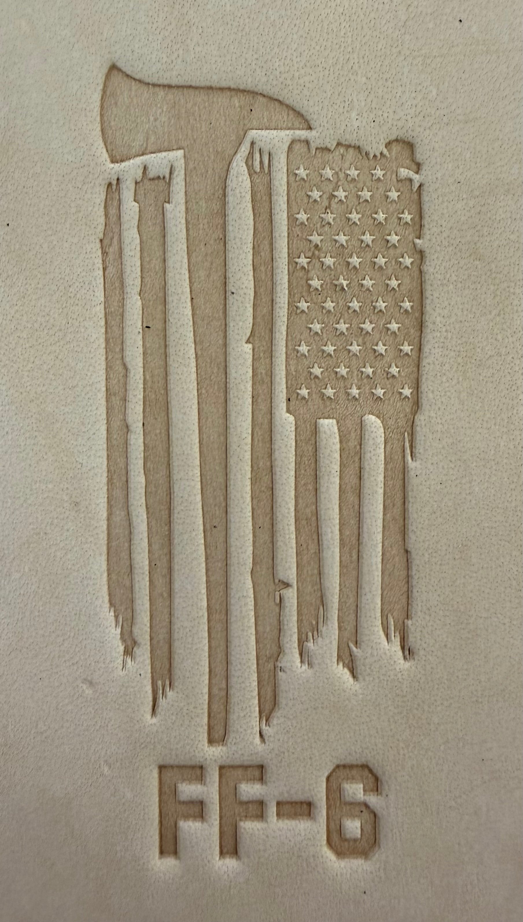 Delrin leather stamp pressing a tattered U.S. flag design with a firefighting axe and Halligan bar into leather.