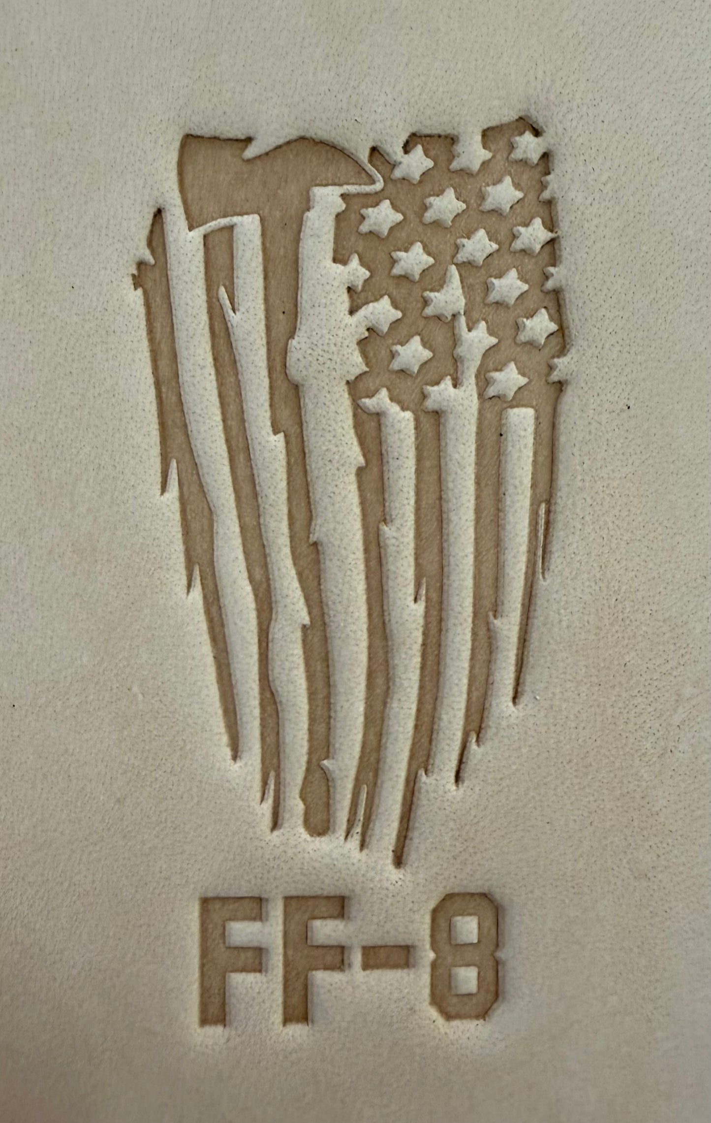 Delrin leather stamp pressing a tattered U.S. flag design with a firefighting axe and Halligan bar into leather.
