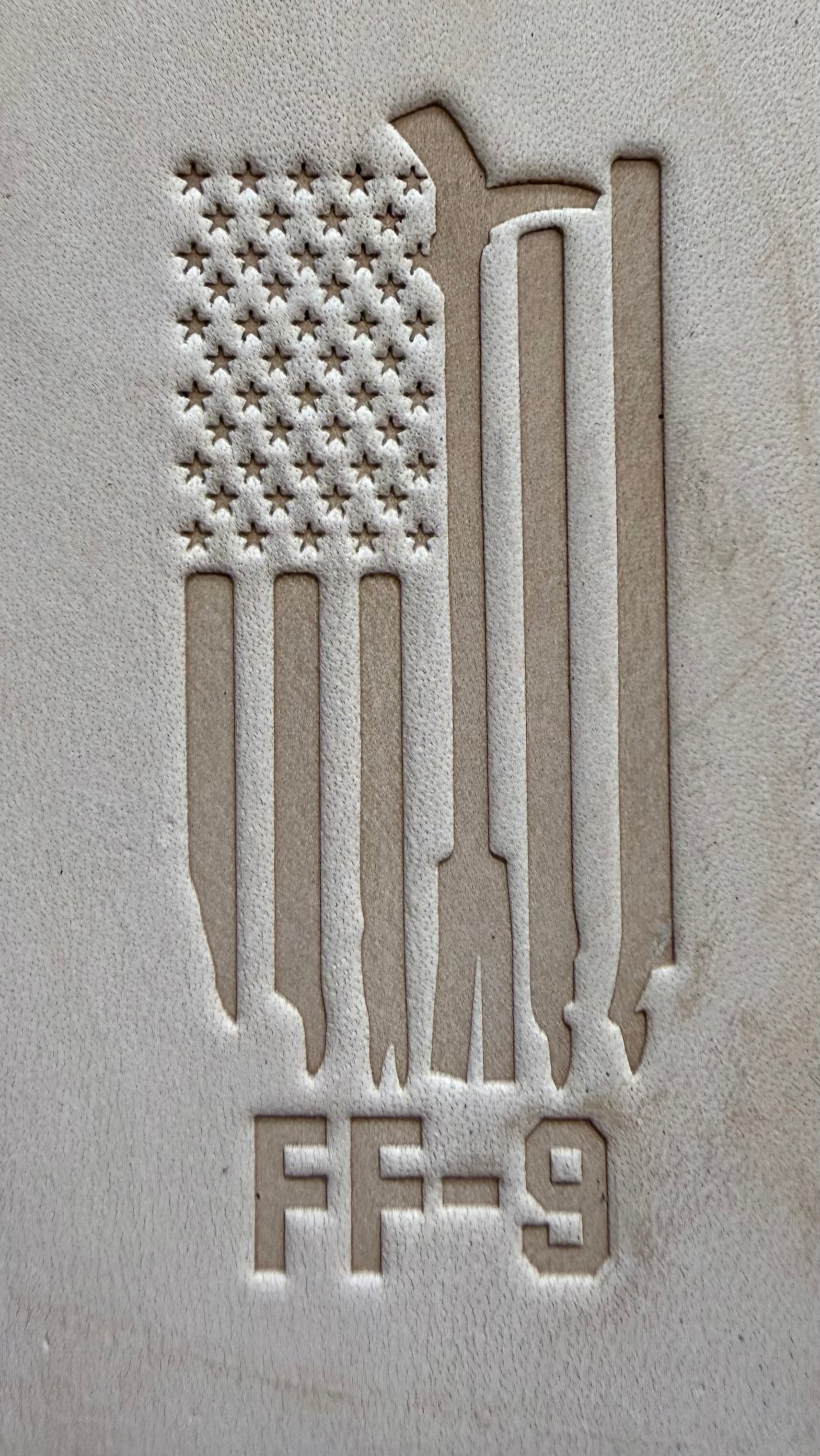 Delrin leather stamp pressing a tattered U.S. flag design with a firefighting axe and Halligan bar into leather.