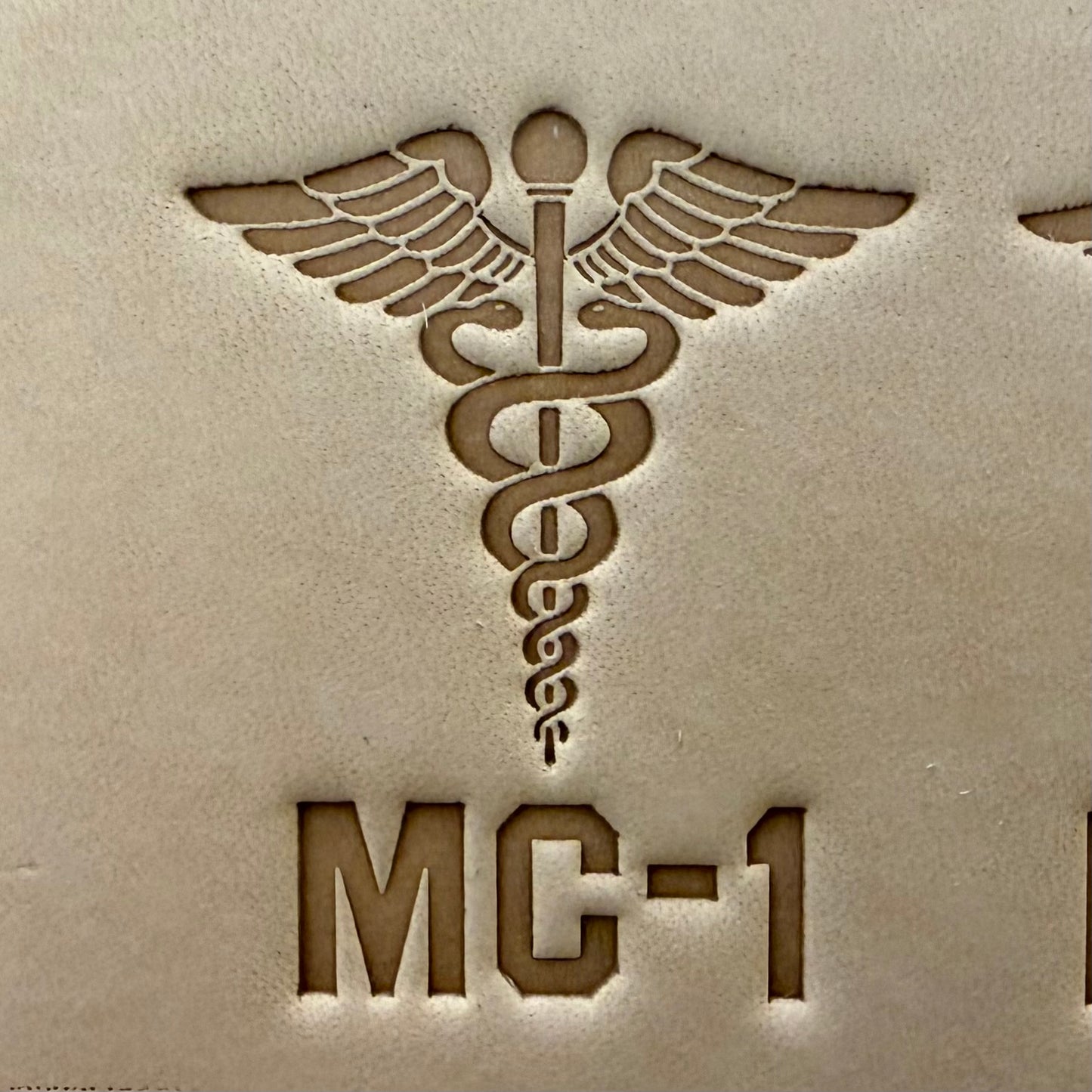 Leathercrafting impression of a medical caduceus symbol.