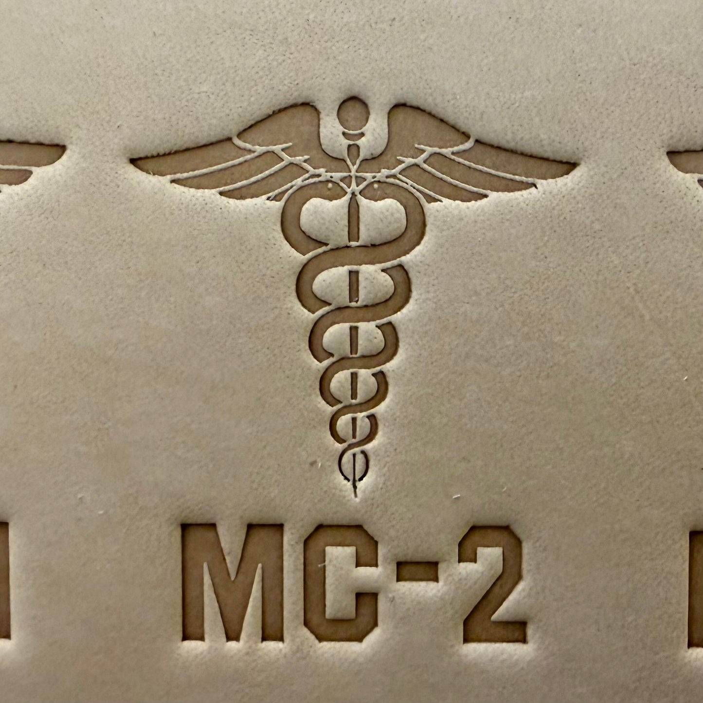 Leathercrafting impression of a medical caduceus symbol.