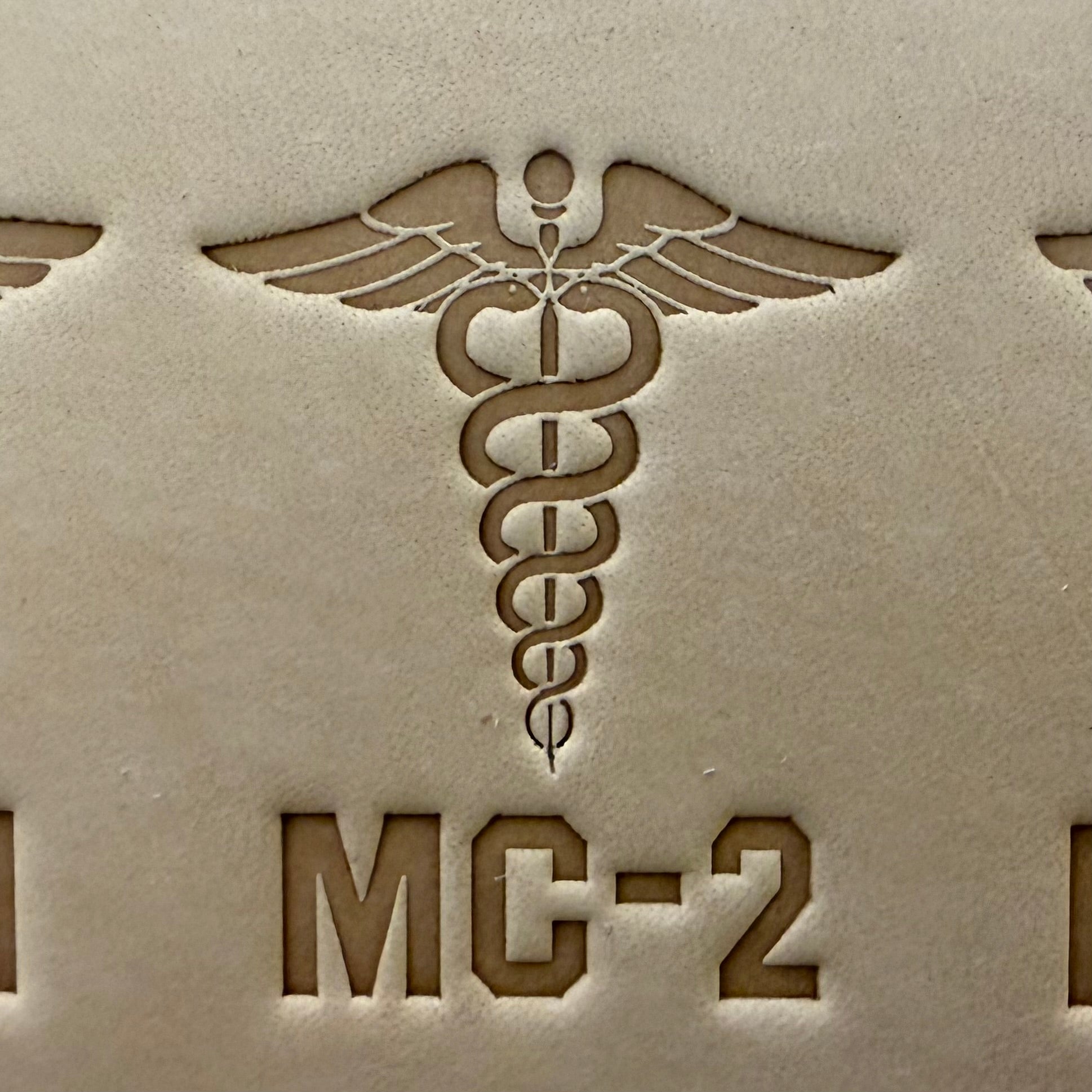 Leathercrafting impression of a medical caduceus symbol.