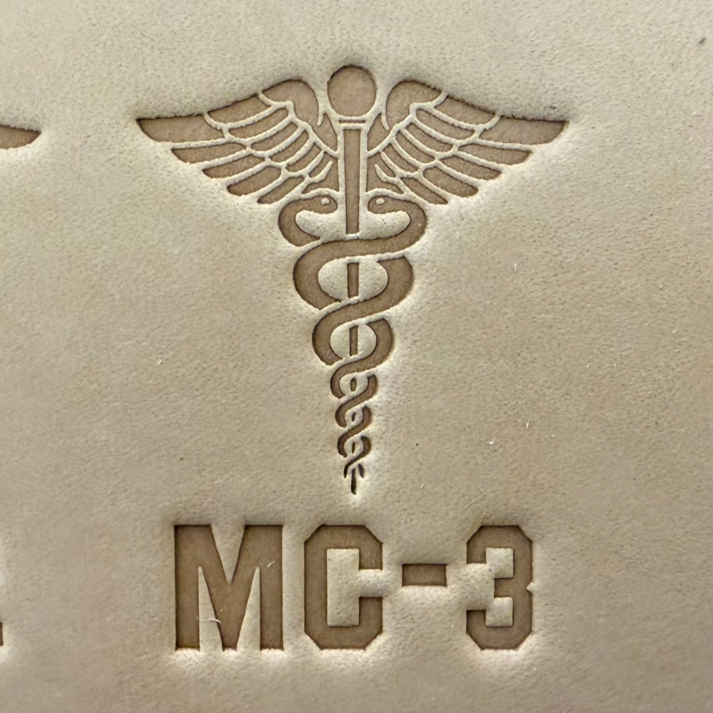 Leathercrafting impression of a medical caduceus symbol.
