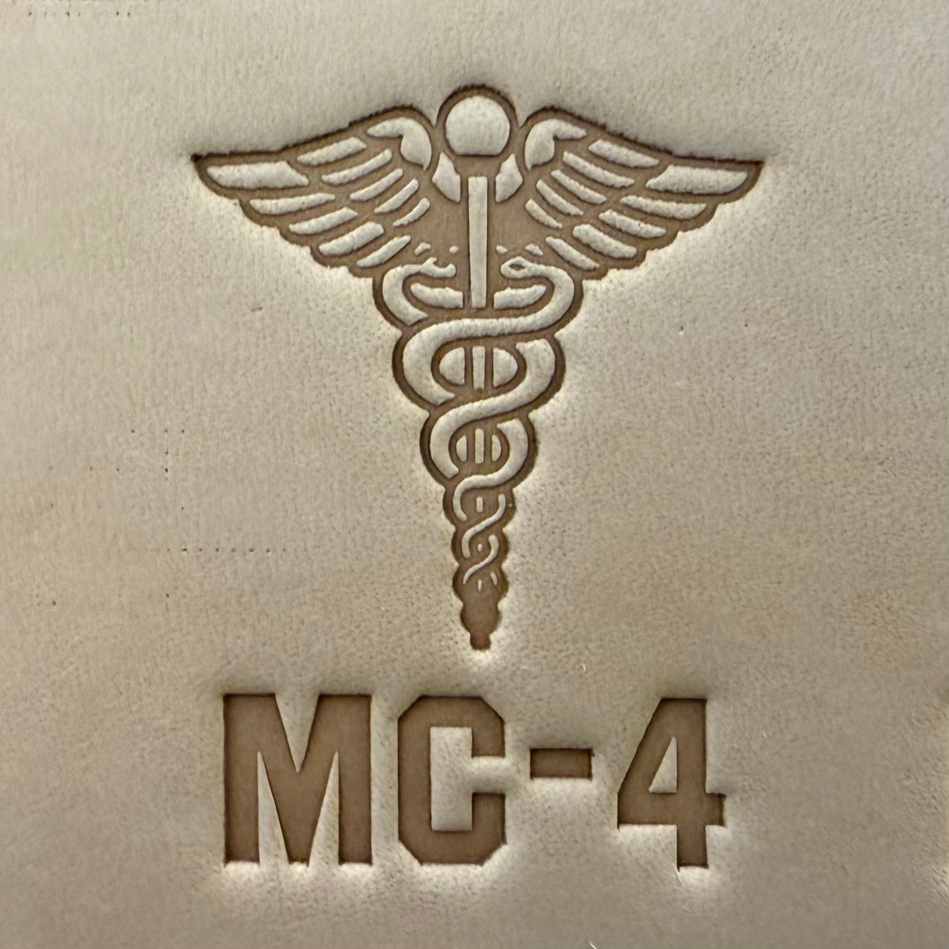 Leathercrafting impression of a medical caduceus symbol.